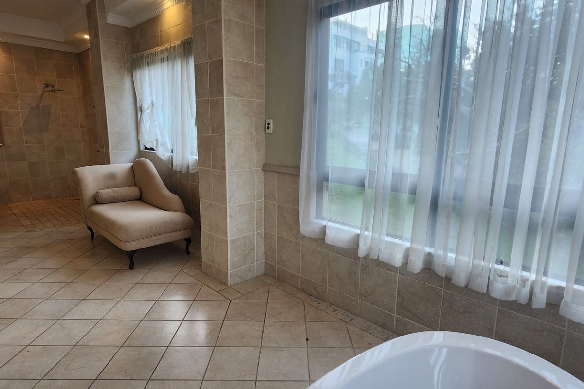 Spacious bathroom featuring neutral floor-to-ceiling tiling, a freestanding bathtub, a separate shower area, and a bidet, offering a functional and well-lit layout.