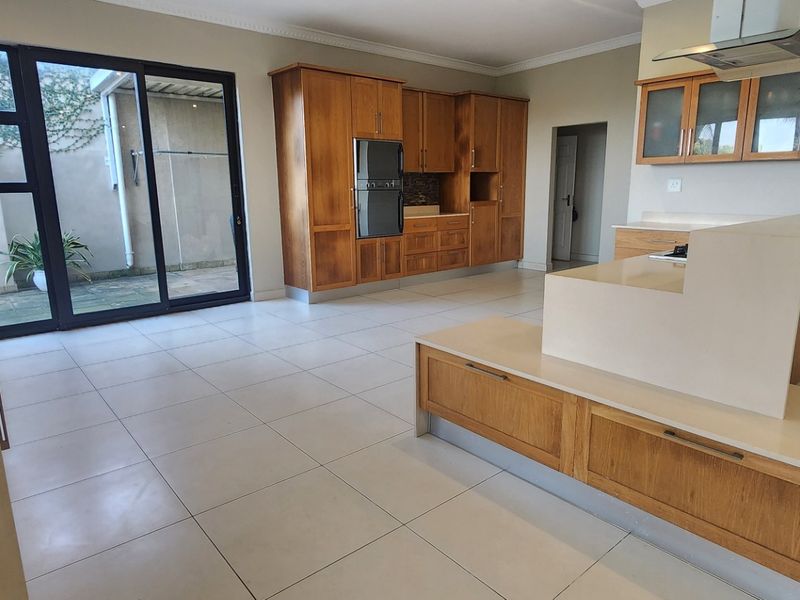 Spacious kitchen featuring wooden cabinetry, stone countertops, built-in oven, and extractor fan, with direct access to an outdoor patio area.
