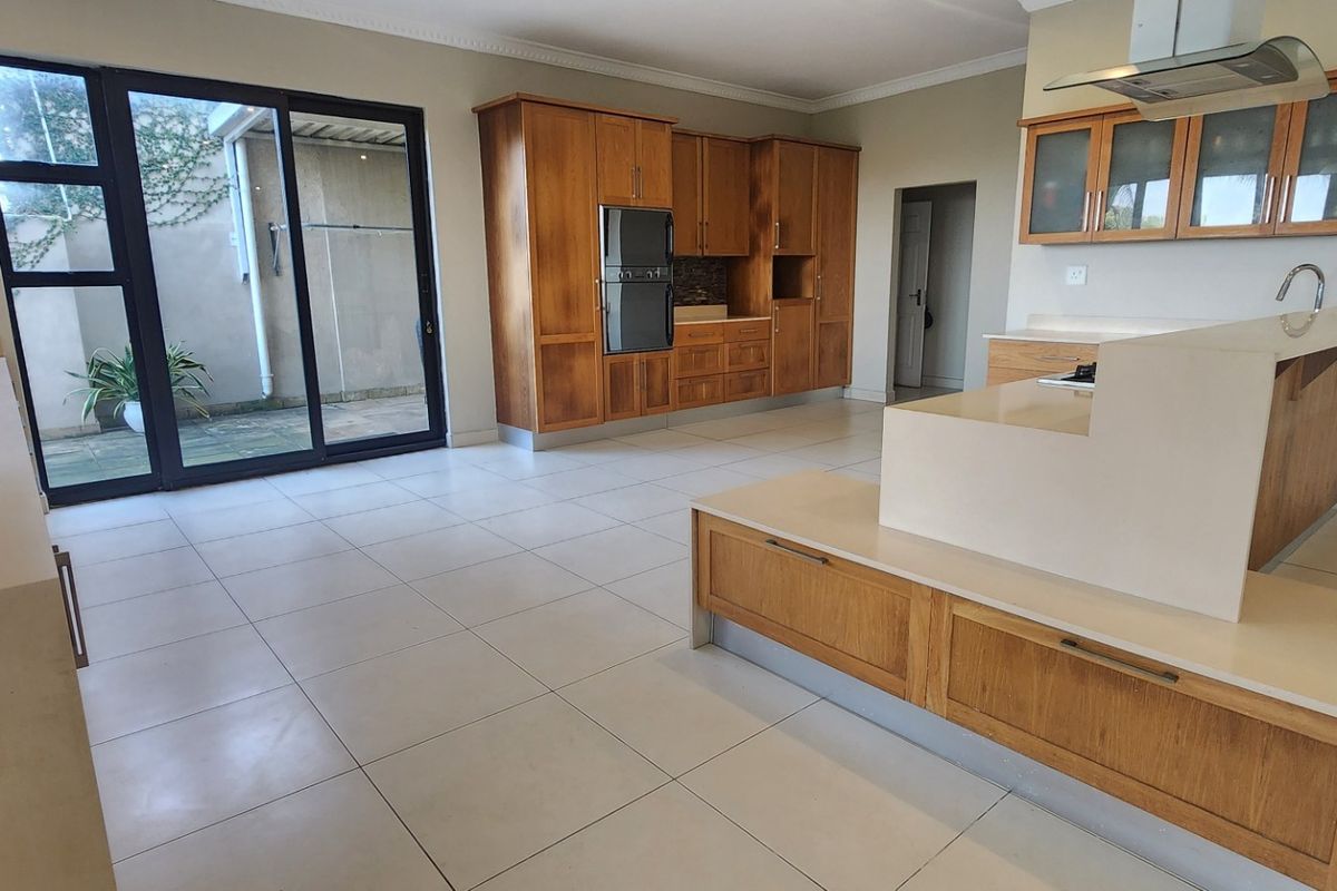 Spacious kitchen featuring wooden cabinetry, stone countertops, built-in oven, and extractor fan, with direct access to an outdoor patio area.