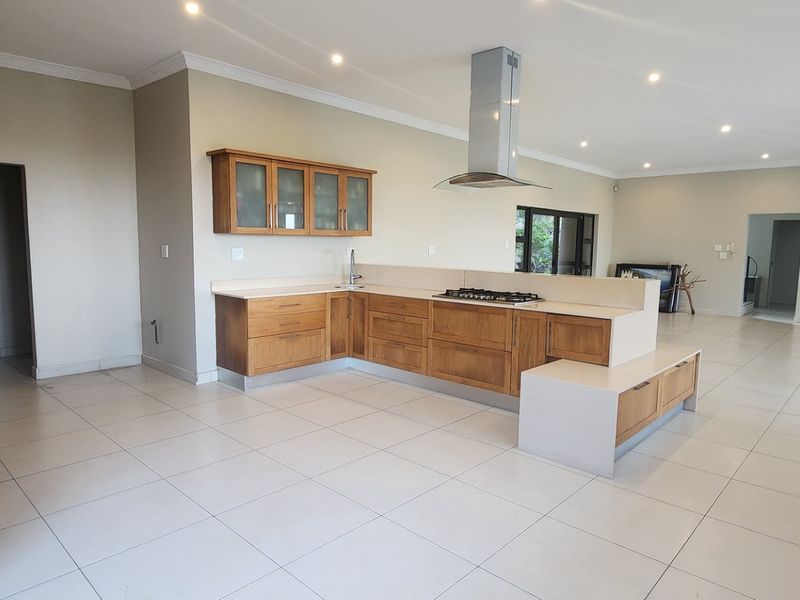 Spacious open-plan kitchen featuring wooden cabinetry, stone countertops, and a gas hob, seamlessly flowing into the living area with tiled flooring throughout.