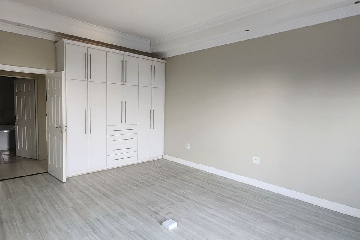 A spacious, empty bedroom featuring neutral walls, modern laminate flooring, built-in white cabinetry, and decorative ceiling cornicing.