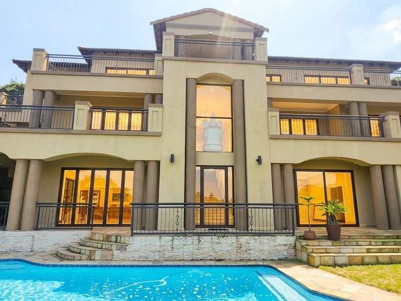 Impressive multi-story rear elevation featuring expansive balconies, large glass sliding doors, and a well-maintained swimming pool with stone-clad retaining walls.
