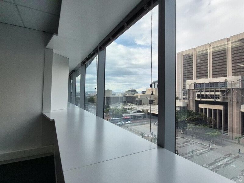 An empty office space featuring large windows with an urban city view and a suspended ceiling.