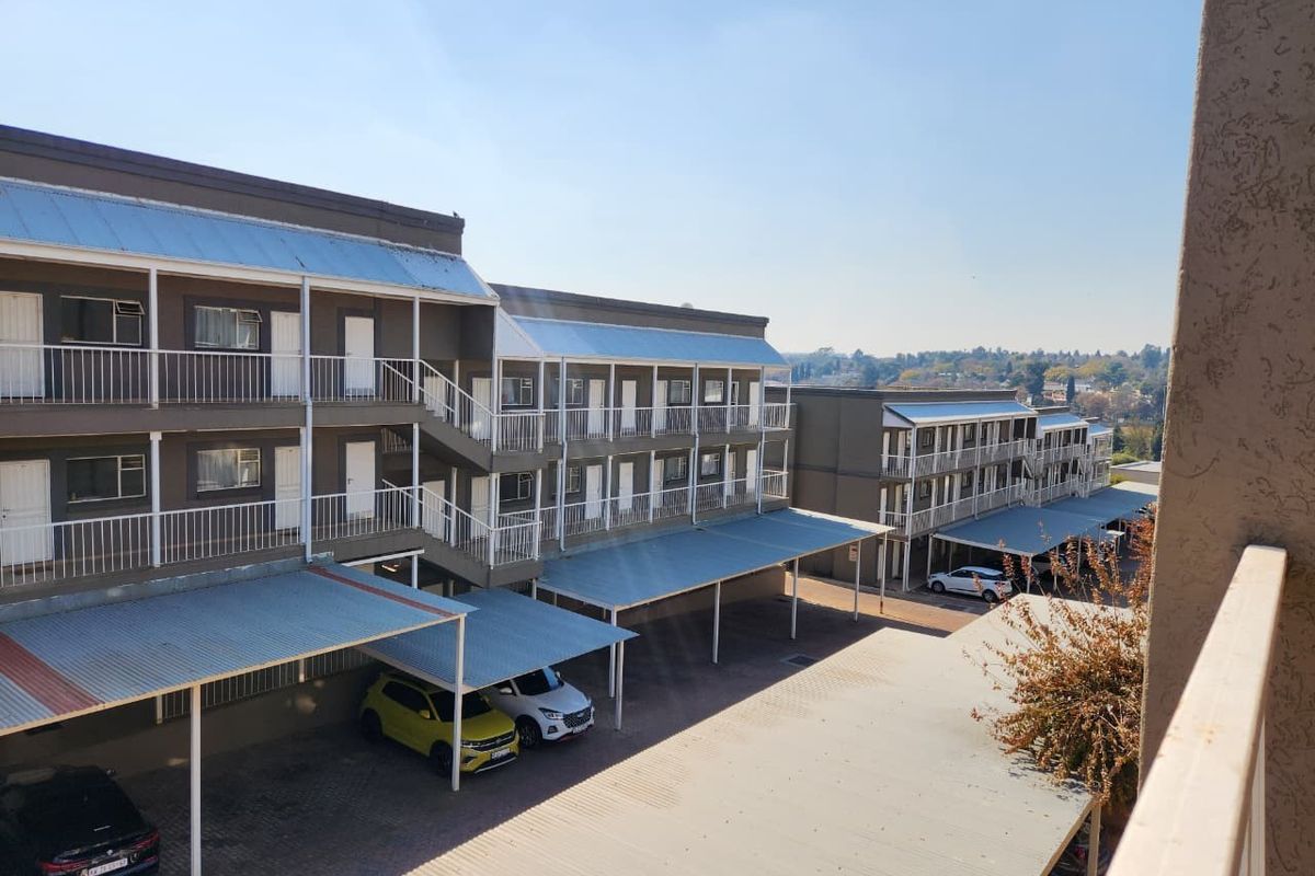 Exterior view of an apartment complex featuring multi-level balconies, covered parking bays, and paved driveway access.