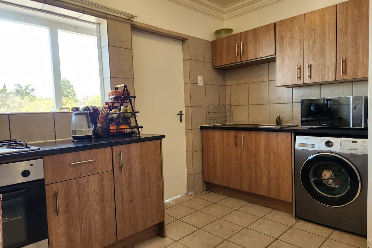 Functional kitchen featuring wood-finish cabinetry, granite countertops, tiled backsplash, and integrated appliances including an oven, hob, and laundry connection.