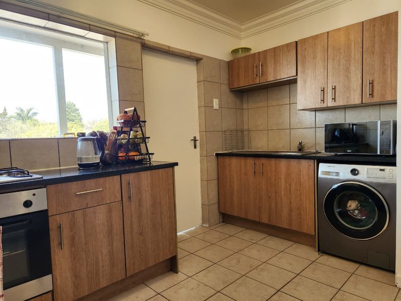 Functional kitchen featuring wood-finish cabinetry, granite countertops, tiled backsplash, and integrated appliances including an oven, hob, and laundry connection.