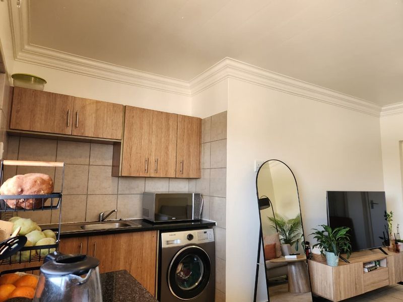 Open-plan living area featuring a compact kitchen with laminate cabinetry, granite countertops, and an integrated washing machine, flowing into the adjacent lounge space.