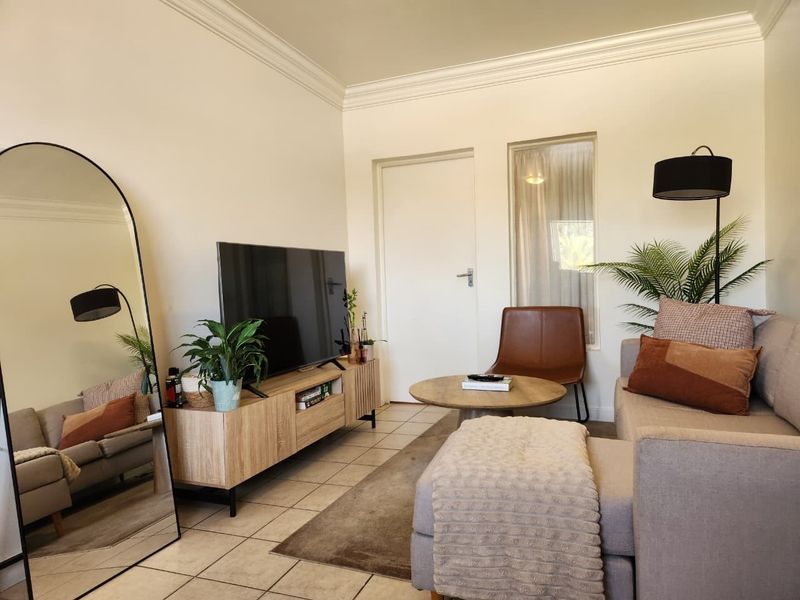 A well-maintained living room featuring neutral tiled flooring, classic crown molding, and a bright, functional layout.