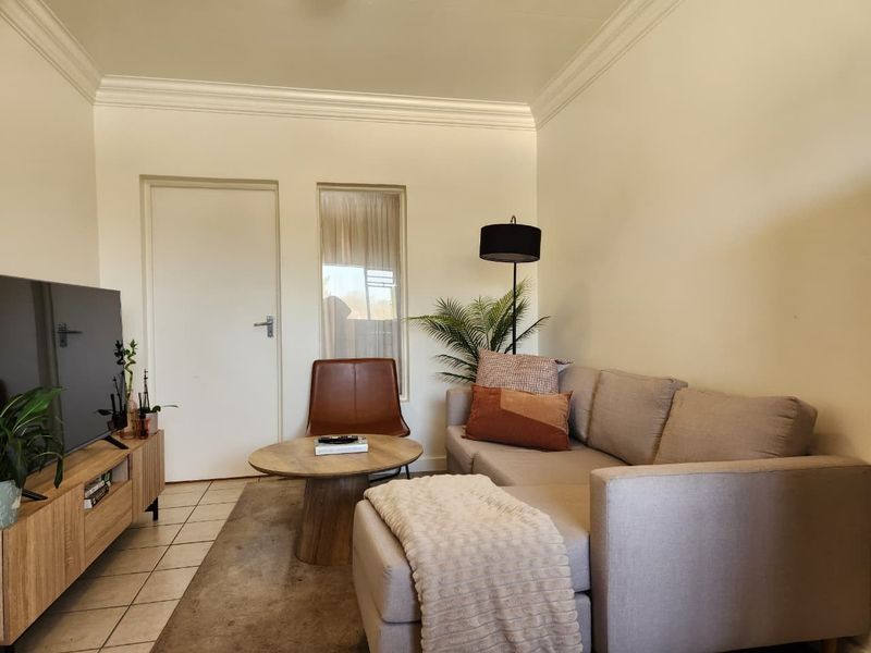 A cozy living room featuring tiled flooring, crown molding, and a neutral color palette, providing a comfortable and well-maintained space.