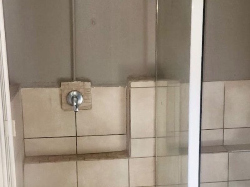 A functional shower stall featuring a glass enclosure, tiled walls, and a built-in shower base, requiring minor cosmetic updates to improve its overall appearance.