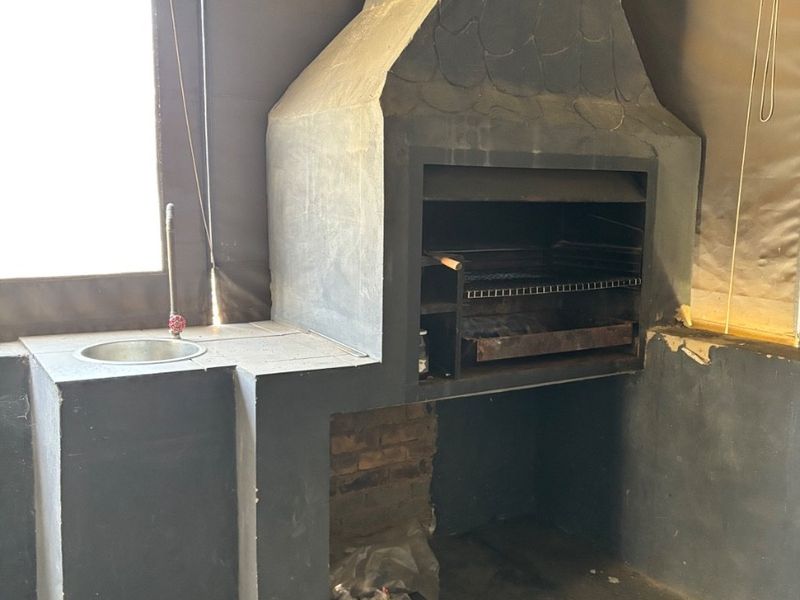 Covered patio area featuring a built-in braai and integrated sink, with canvas blinds and concrete flooring.