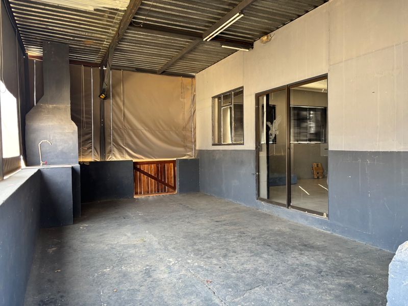 A covered outdoor patio area featuring a built-in braai, concrete flooring, and direct access to the interior through a sliding glass door.