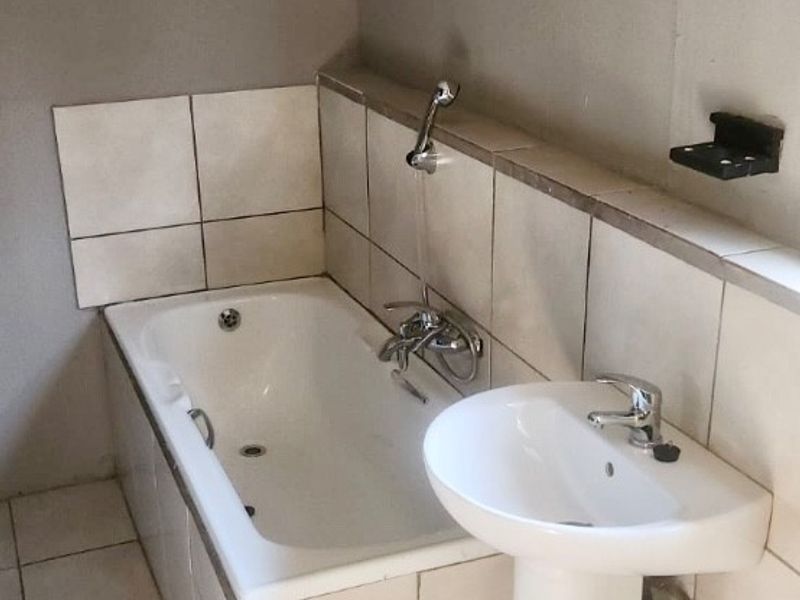 A functional bathroom featuring a built-in bathtub with a handheld shower attachment and a pedestal basin with tiled finishes.