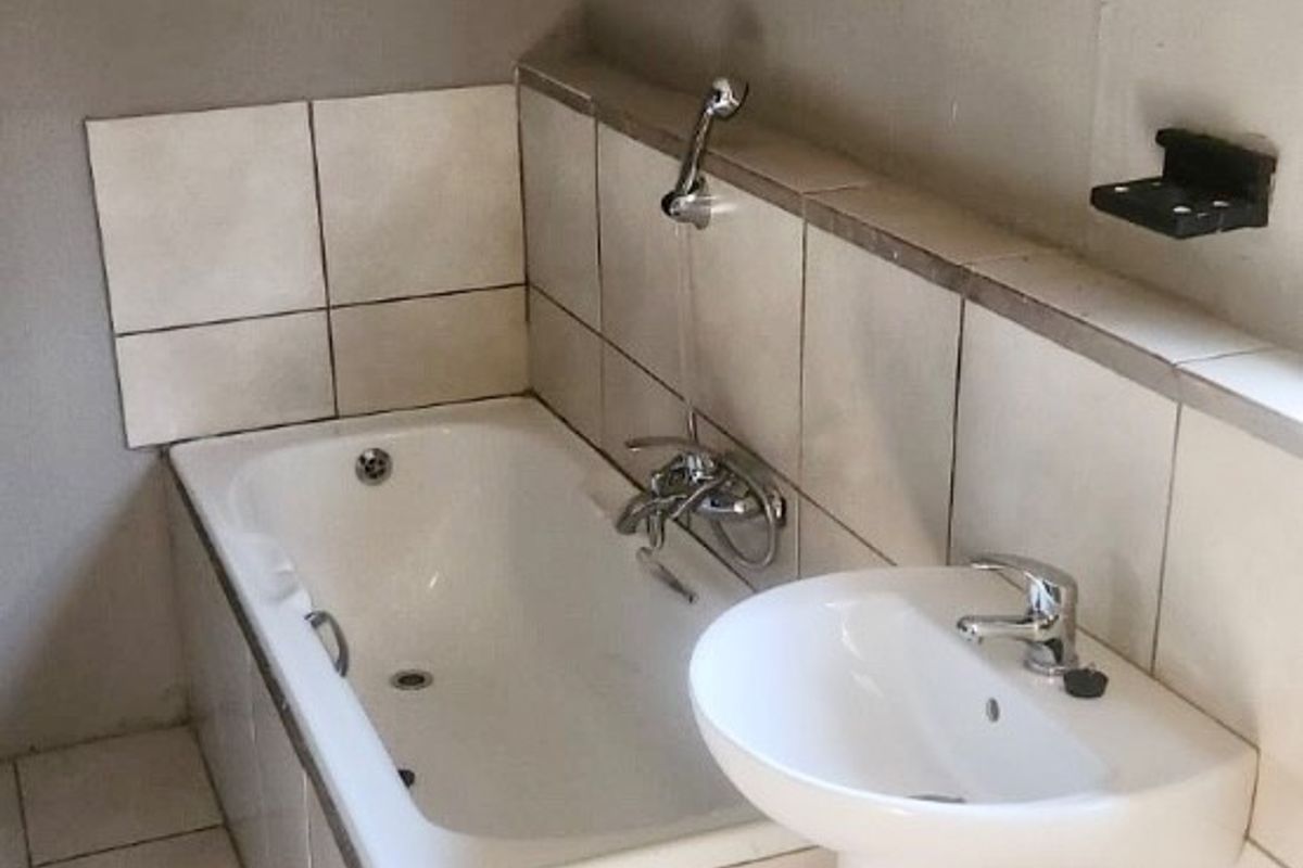 A functional bathroom featuring a built-in bathtub with a handheld shower attachment and a pedestal basin with tiled finishes.