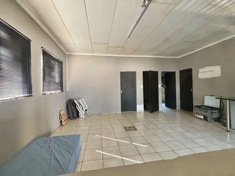 A spacious, empty living area featuring tiled flooring, neutral grey walls, and multiple access doors, offering a blank canvas for renovation.