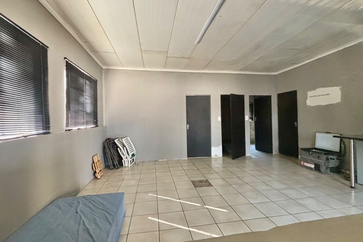 A spacious, empty living area featuring tiled flooring, neutral grey walls, and multiple access doors, offering a blank canvas for renovation.