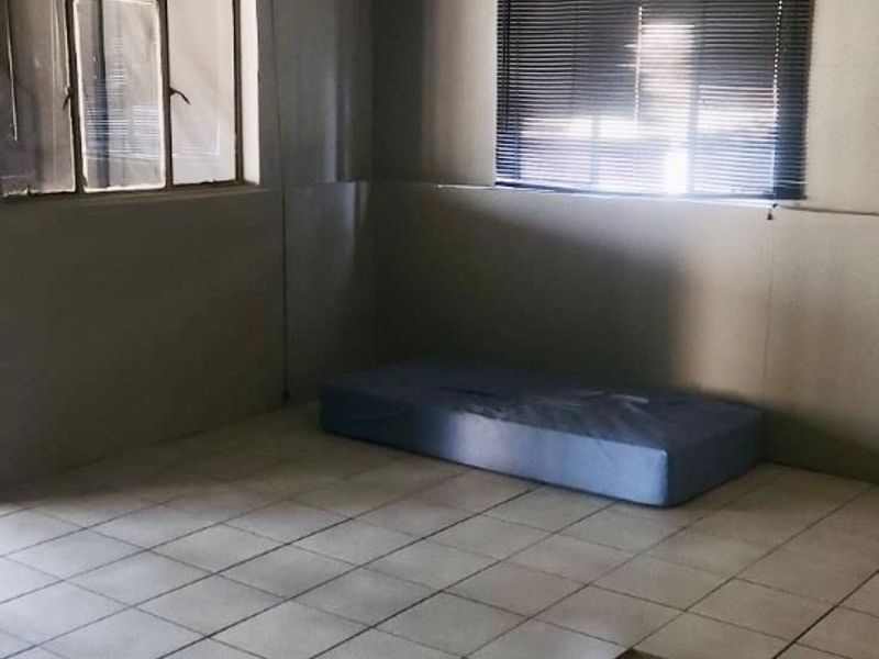 An empty bedroom featuring tiled flooring with a missing tile and venetian blinds on the windows.