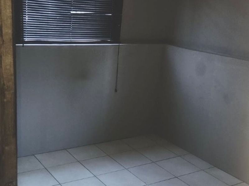 An empty bedroom featuring tiled flooring, grey painted walls, and venetian blinds, offering a blank canvas for potential interior design updates.