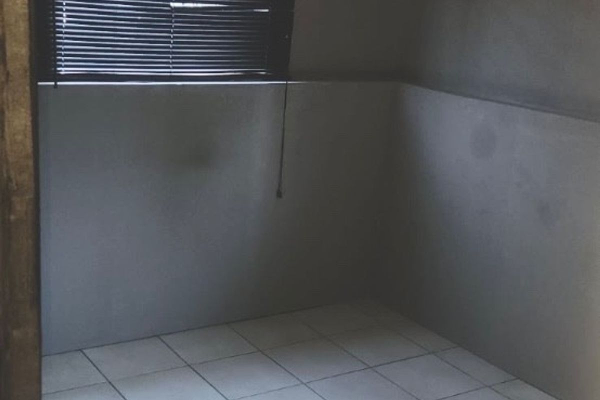 An empty bedroom featuring tiled flooring, grey painted walls, and venetian blinds, offering a blank canvas for potential interior design updates.