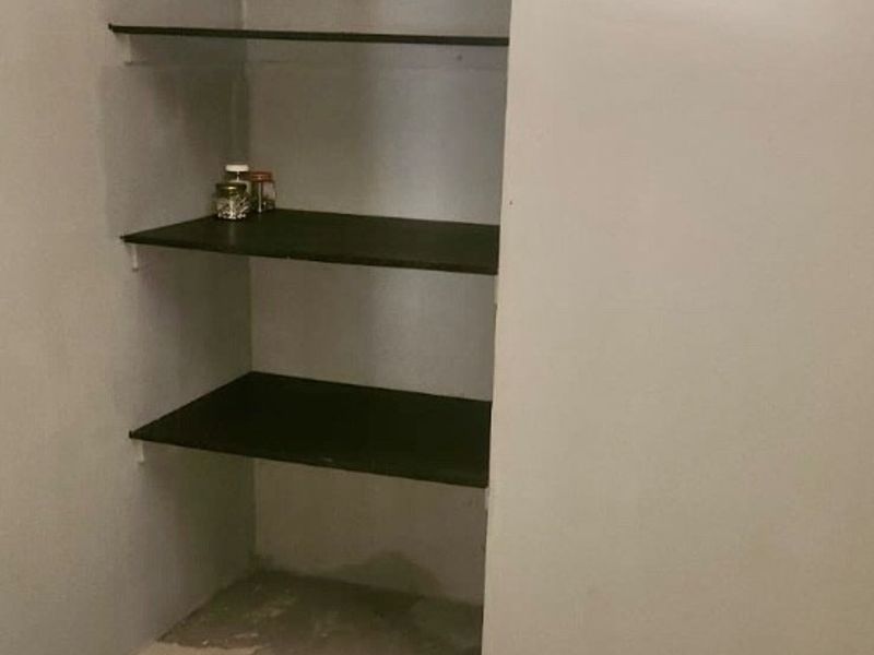 A small utility or pantry area featuring built-in shelving and tiled flooring, requiring minor finishing work to complete the space.