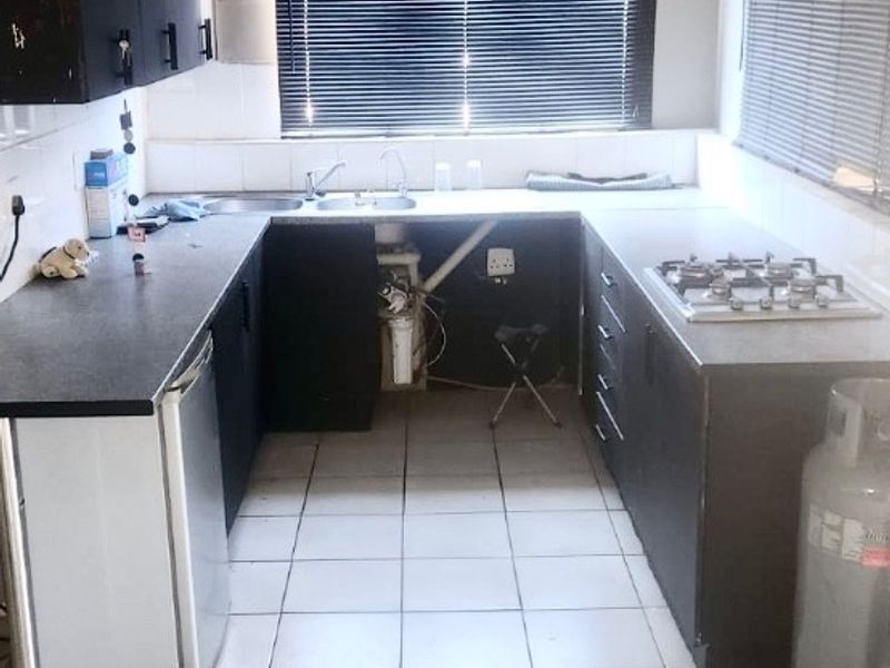 A functional kitchen featuring dark cabinetry, a gas hob, and tiled flooring. The space requires cosmetic updates and ceiling repairs to improve its overall condition.
