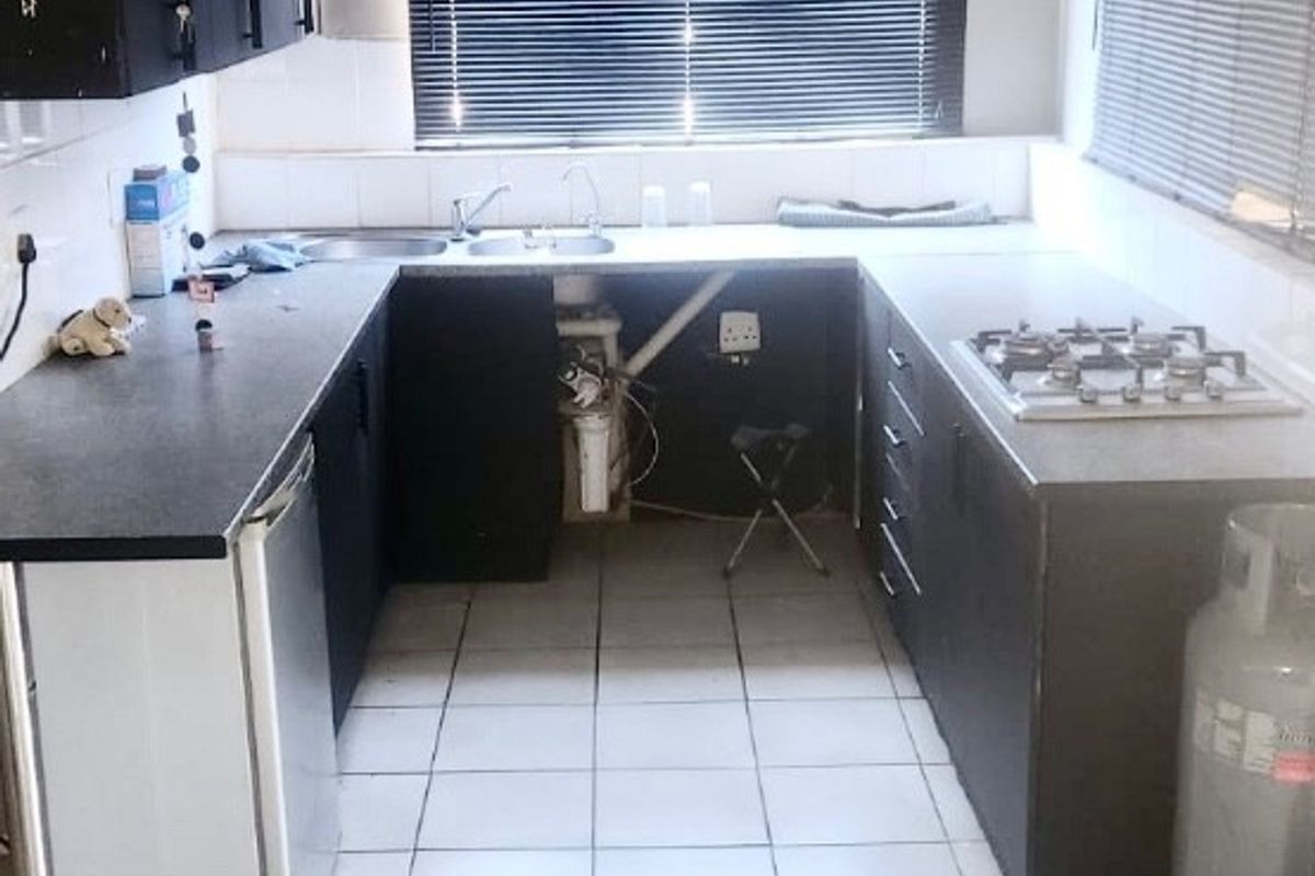 A functional kitchen featuring dark cabinetry, a gas hob, and tiled flooring. The space requires cosmetic updates and ceiling repairs to improve its overall condition.