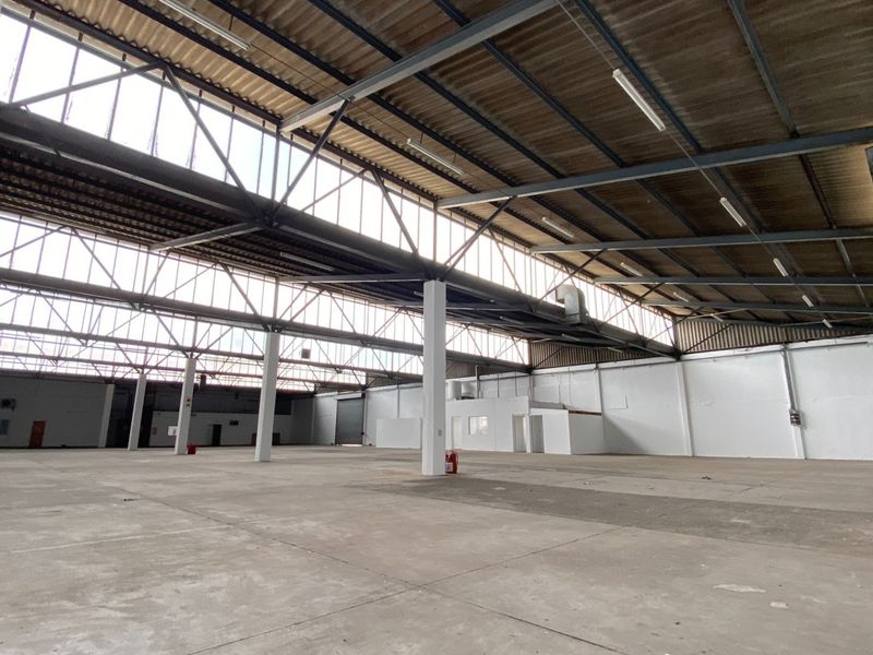 Spacious industrial warehouse featuring high ceilings with exposed steel trusses, concrete flooring, and ample natural light from clerestory windows.