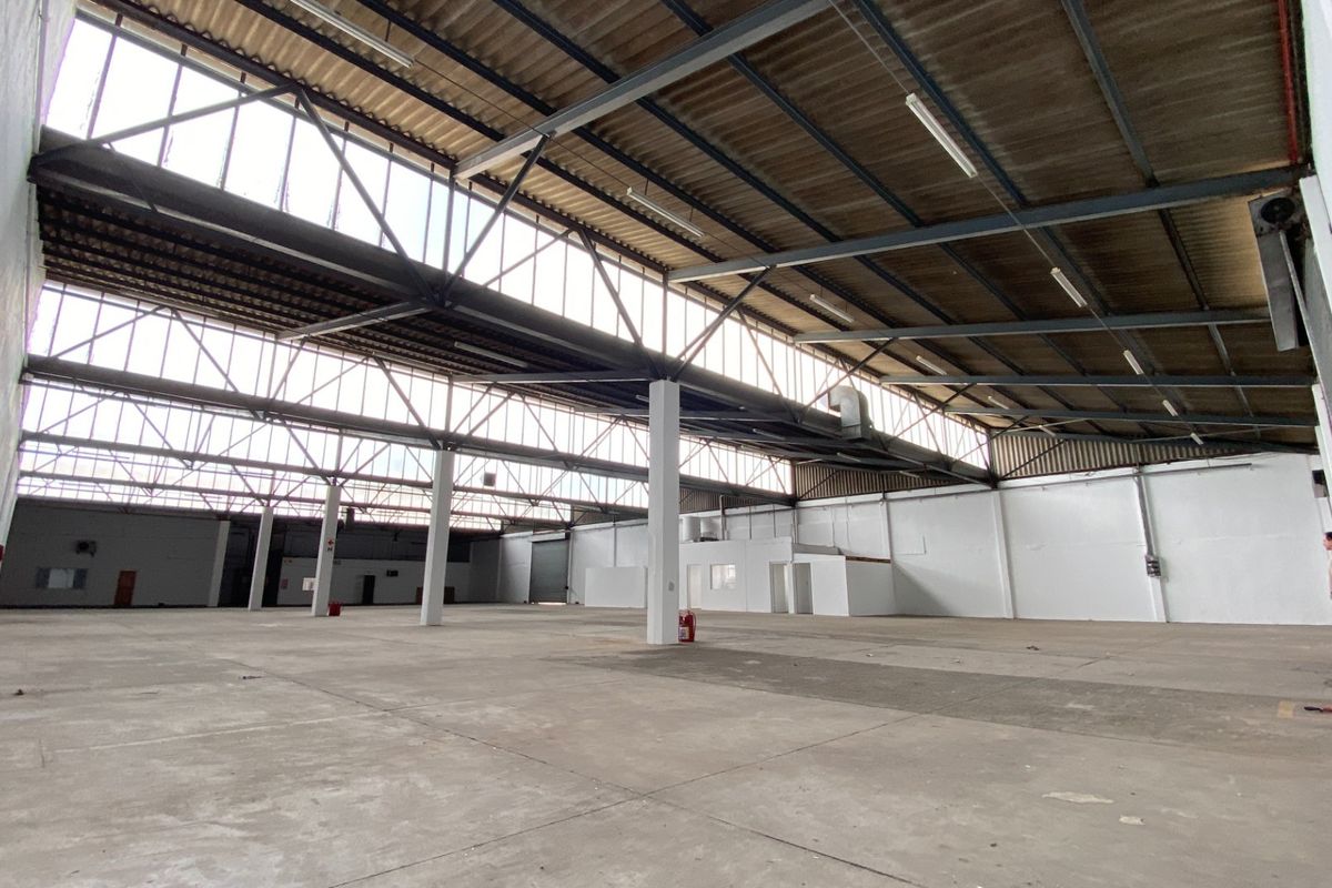 Spacious industrial warehouse featuring high ceilings with exposed steel trusses, concrete flooring, and ample natural light from clerestory windows.