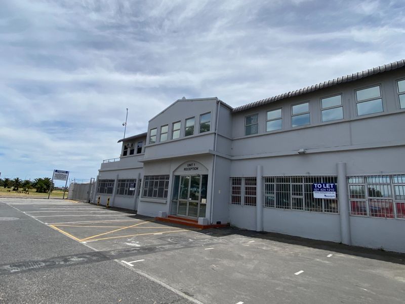 Front exterior view of an industrial unit featuring a paved parking area, security-barred windows, and a dedicated reception entrance.