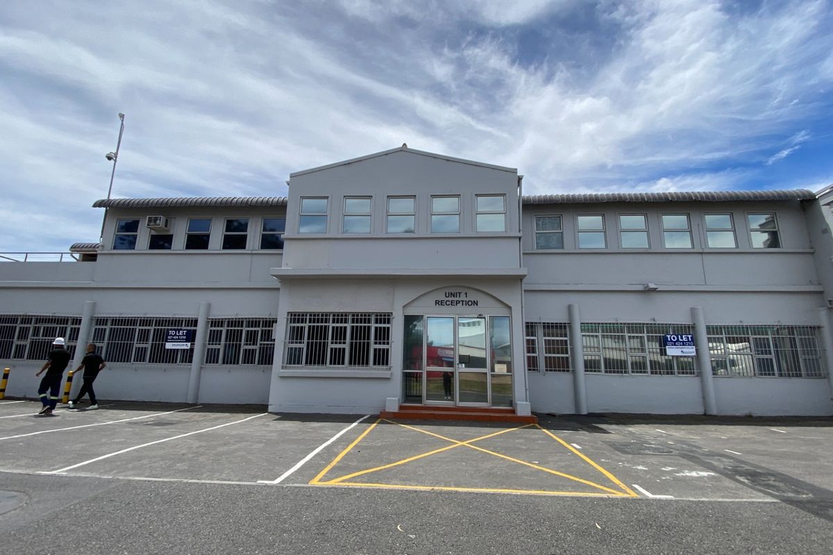 Front elevation of an industrial unit featuring a dedicated reception entrance, security-barred windows, and an asphalt-paved parking area.