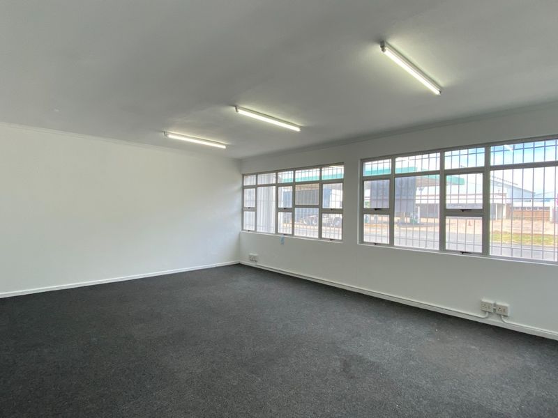 A clean, empty office space featuring carpeted flooring, large windows with security bars, and functional overhead fluorescent lighting.