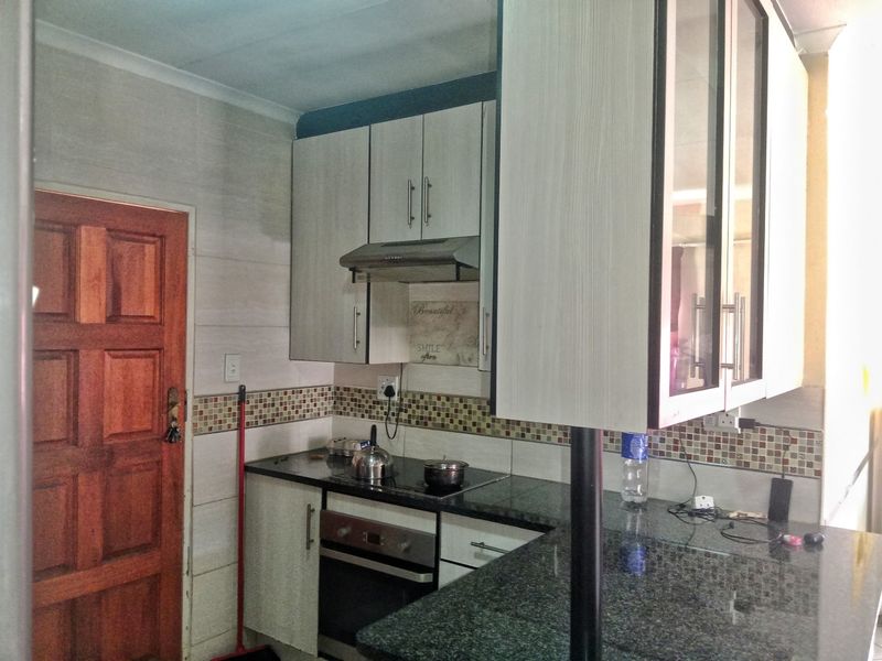 Compact kitchen featuring built-in cabinetry, granite countertops, an electric hob with extractor fan, and a breakfast bar area.