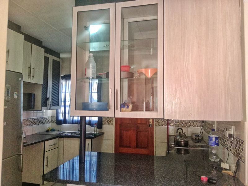 A functional kitchen featuring granite countertops, mosaic tile backsplash, and a mix of laminate and glass-fronted cabinetry with an integrated breakfast bar.