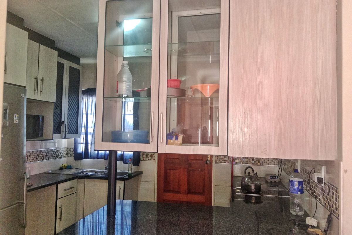 A functional kitchen featuring granite countertops, mosaic tile backsplash, and a mix of solid and glass-front cabinetry with integrated cooking and sink areas.