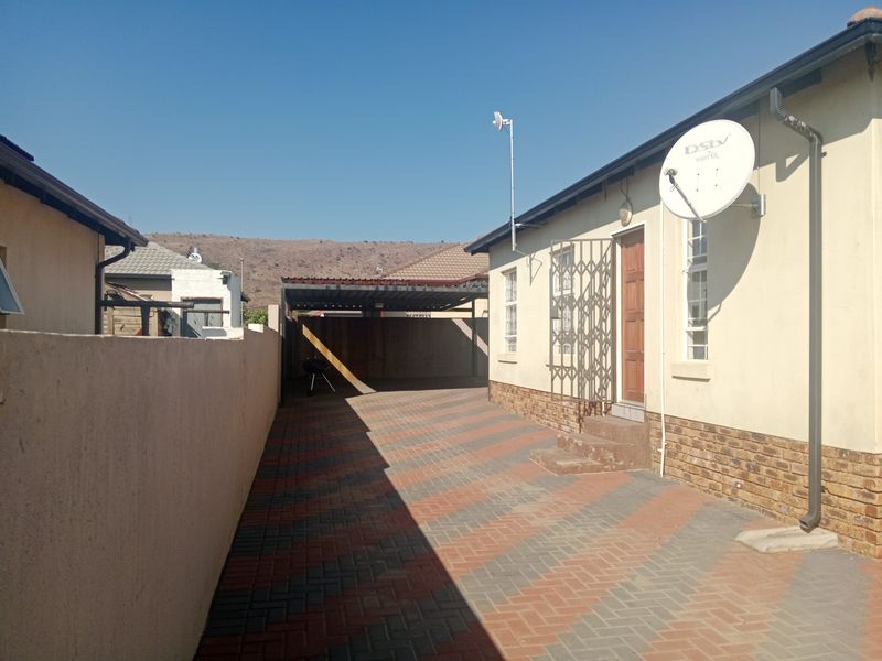 Rear exterior view showing a paved driveway, carport, and side access to the house with a security gate and satellite dish installed.