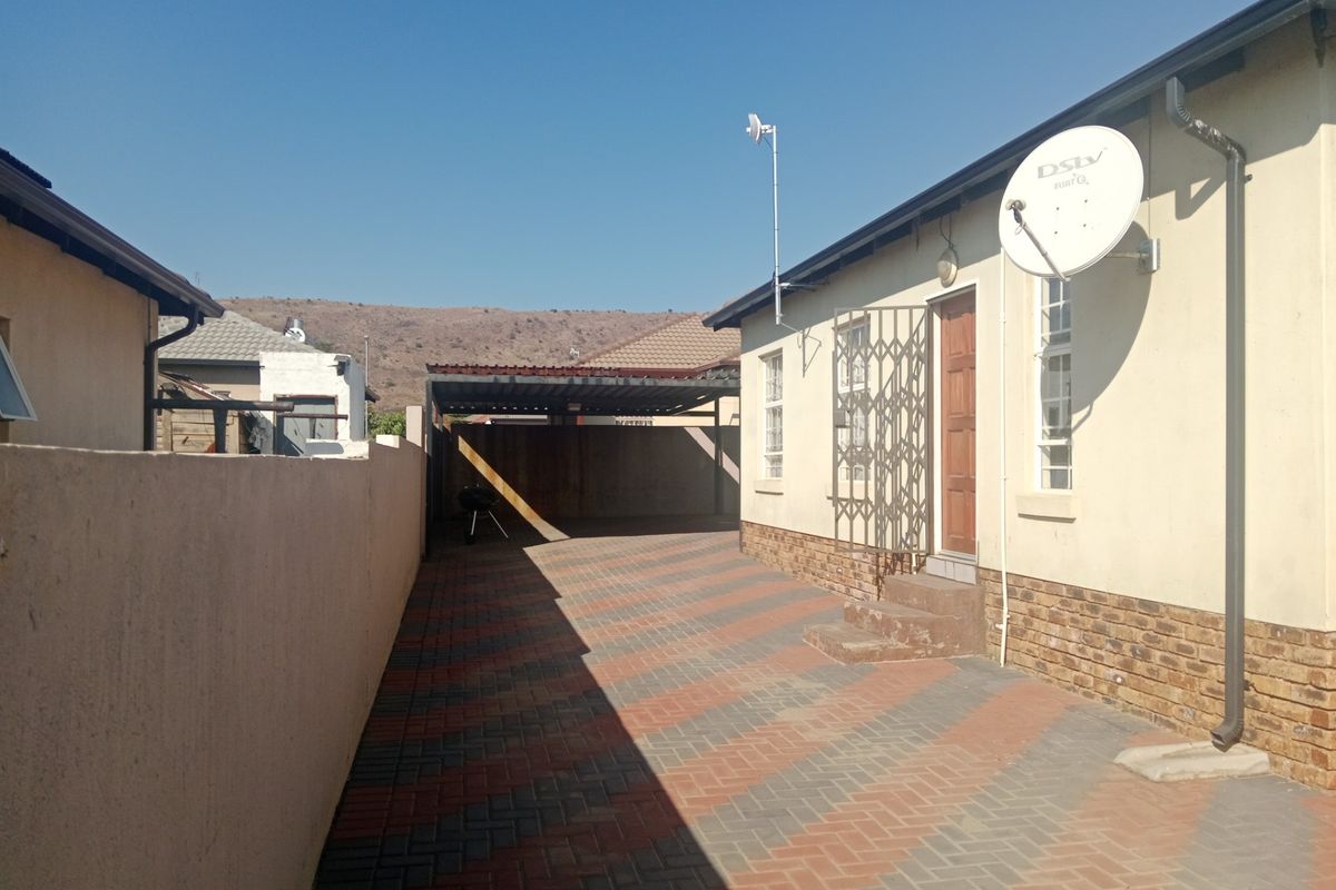 Rear exterior view showing a paved driveway, carport, and side access to the house with a security gate and satellite dish installed.
