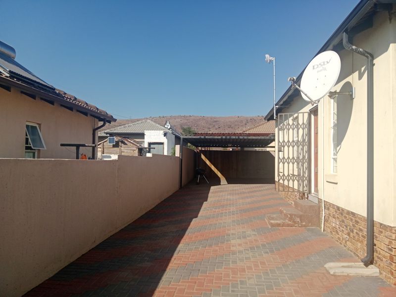 A paved rear driveway area featuring a carport, boundary wall, and security gate access to the main dwelling.