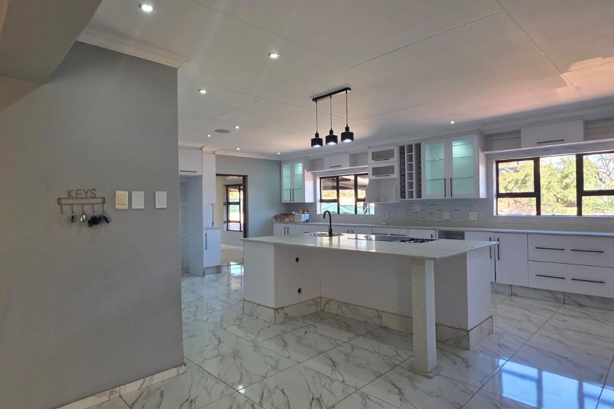 Modern, spacious kitchen featuring a large central island, white cabinetry, marble-look tiled flooring, and ample natural light from large windows.