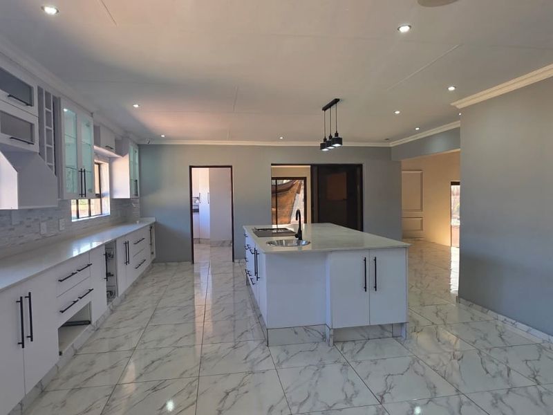Modern, spacious kitchen featuring a large central island, sleek white cabinetry, stone countertops, and high-quality tiled flooring with recessed and pendant lighting.