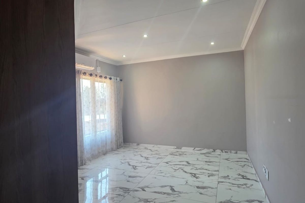 A bright, empty bedroom featuring modern marble-look floor tiles, recessed ceiling lighting, and a wall-mounted air conditioning unit.