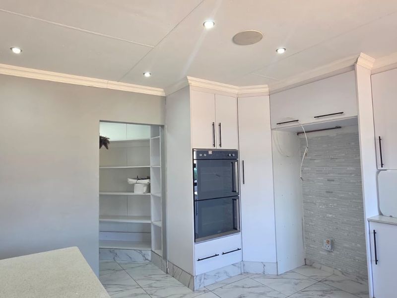 Modern kitchen featuring white cabinetry, built-in double oven, stone countertops, and tiled flooring, with an adjacent walk-in pantry area.
