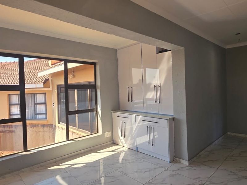 Bright and spacious living area featuring modern white built-in cabinetry, large aluminium windows, and polished marble-look tiled flooring.