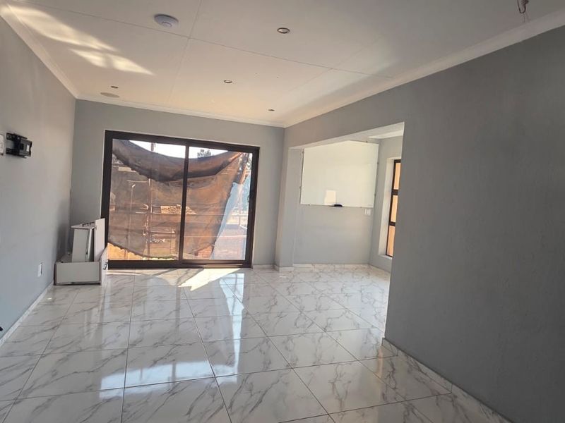 An open-plan living area featuring modern marble-look floor tiles, recessed lighting, and a large sliding glass door leading to the exterior.