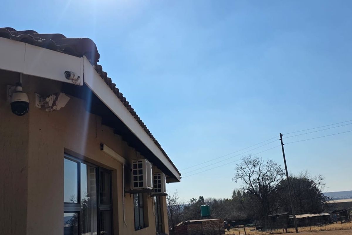 Rear exterior view of the property featuring tiled roofing, mounted security cameras, and external air conditioning units against a clear sky.