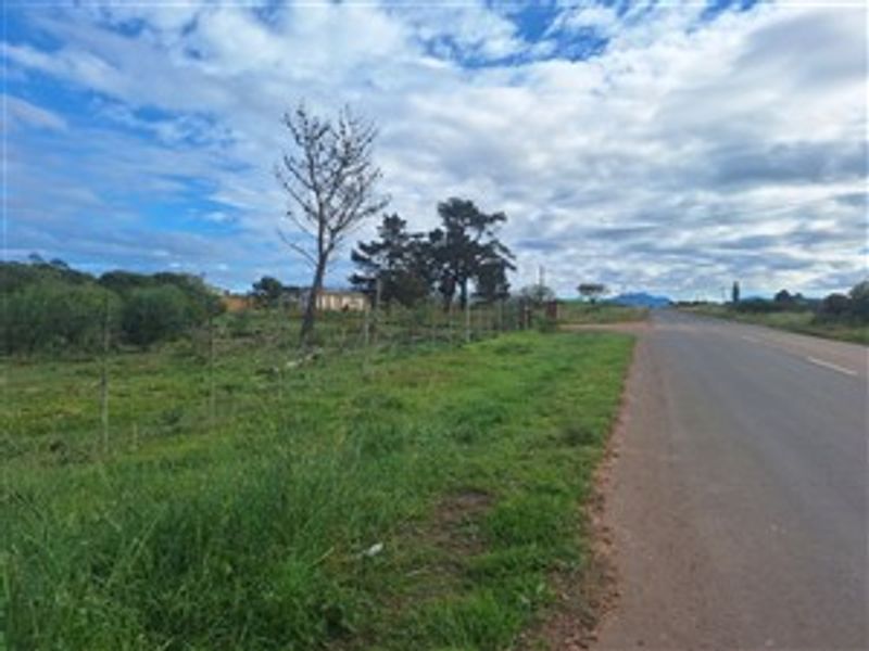 A view of the vacant residential land plot adjacent to the paved public road, featuring natural vegetation and perimeter wire fencing.