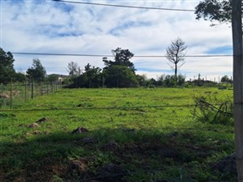 A view of a vacant residential plot featuring open grassland and perimeter wire fencing.
