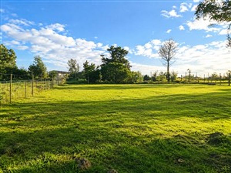 A spacious, level plot of vacant residential land featuring established trees and perimeter wire fencing, offering a clear area for potential development.
