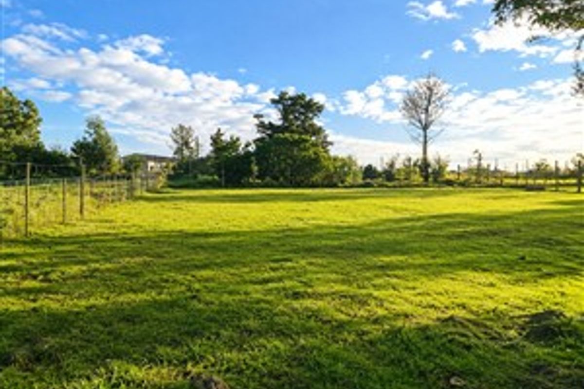 A spacious, level plot of vacant residential land featuring established trees and perimeter wire fencing, offering a clear area for potential development.