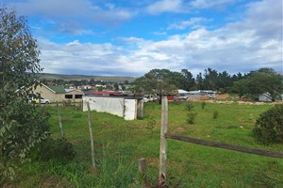 A vacant residential plot featuring a wire fence, wooden posts, and a small, weathered outbuilding structure set against a suburban landscape.