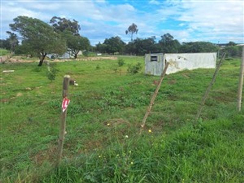 A view of a vacant residential plot featuring grassy terrain, perimeter wire fencing, and a small concrete structure.